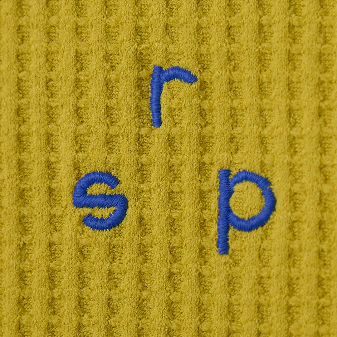 Close-up of the small blue embroidered r s p letters on the mustard waffle knit